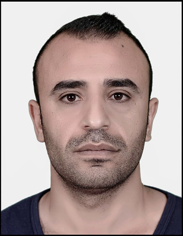 رجل ذو شعر داكن قصير ولحية مشذبة ينظر مباشرة إلى الكاميرا بتعبير محايد، على خلفية فاتحة بسيطة.