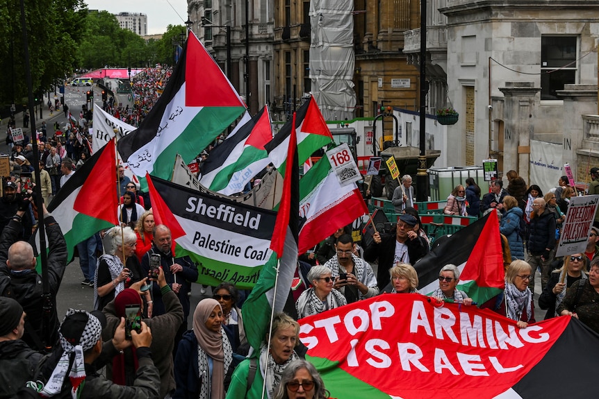 أشخاص يسيرون في أحد الشوارع ويلوحون بالأعلام الفلسطينية ولافتة مكتوب عليها 